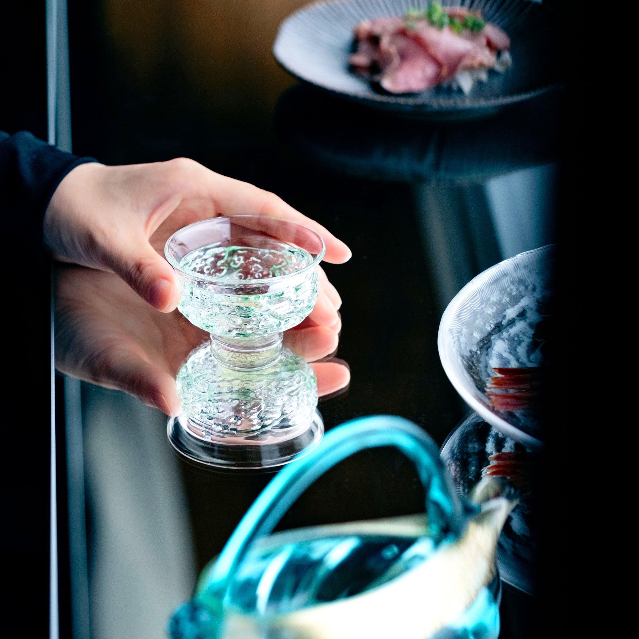 津軽びいどろ 盃12ヶ月コレクション 5月新緑 食卓に並ぶ盃を手でつかんでいる画像