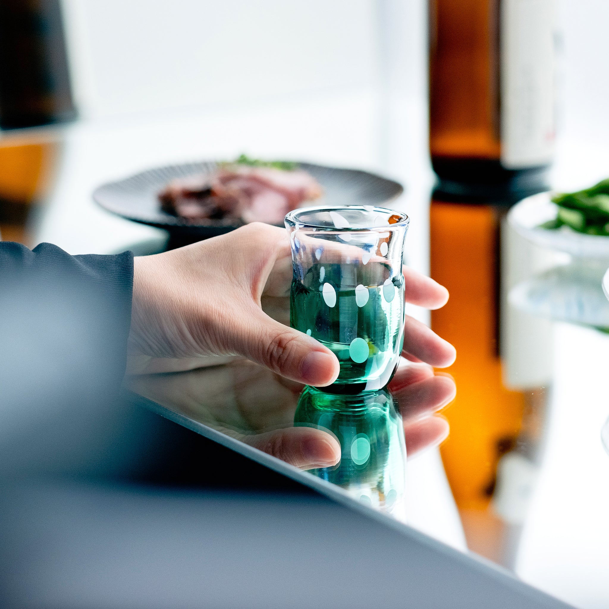 津軽びいどろ 盃12ヶ月コレクション 6月梅雨晴 食卓に並ぶ盃を手でつかんでいる画像