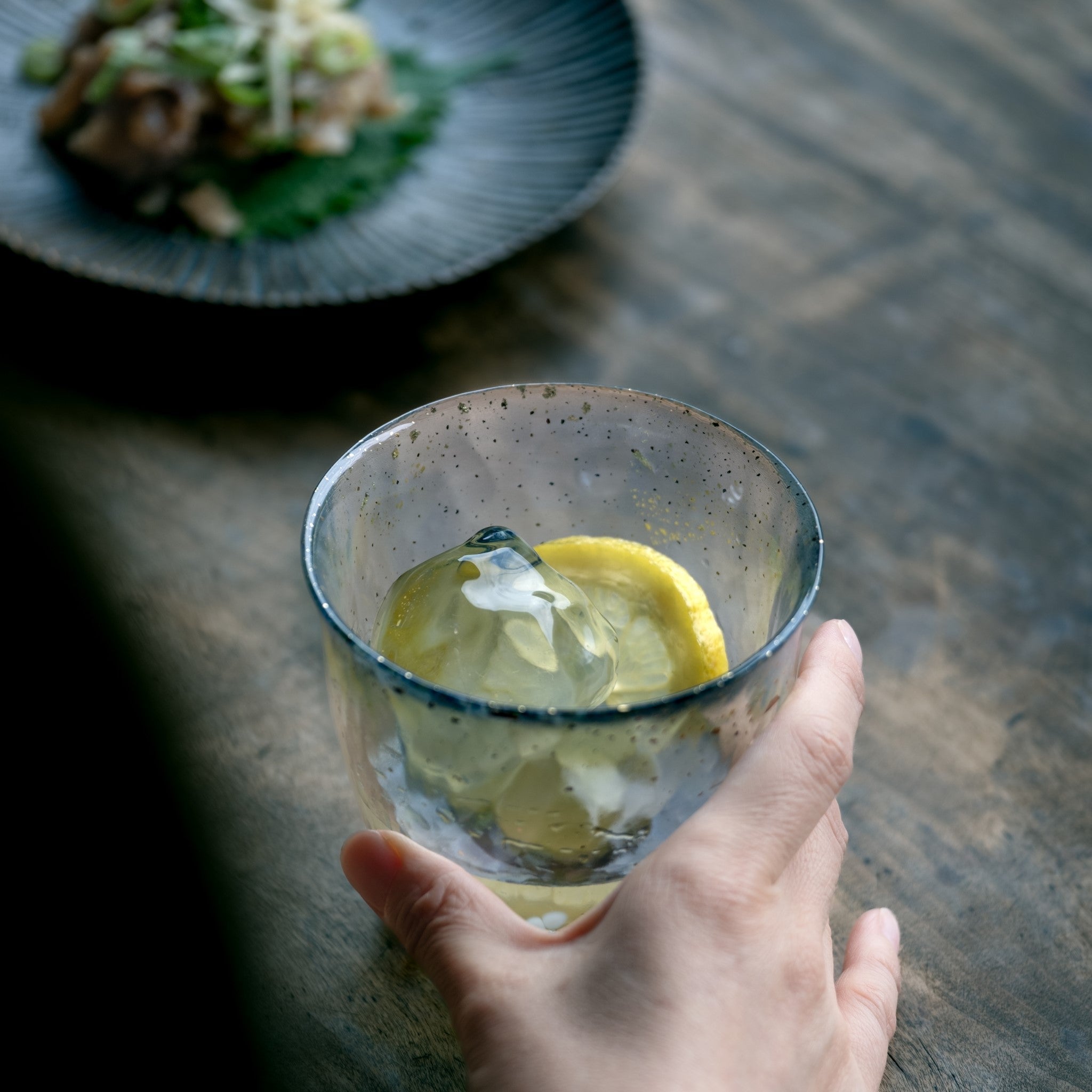 津軽びいどろ 氷華 金彩ロックグラス雫 レモン水が入ったグラスを手でつかんでいる画像