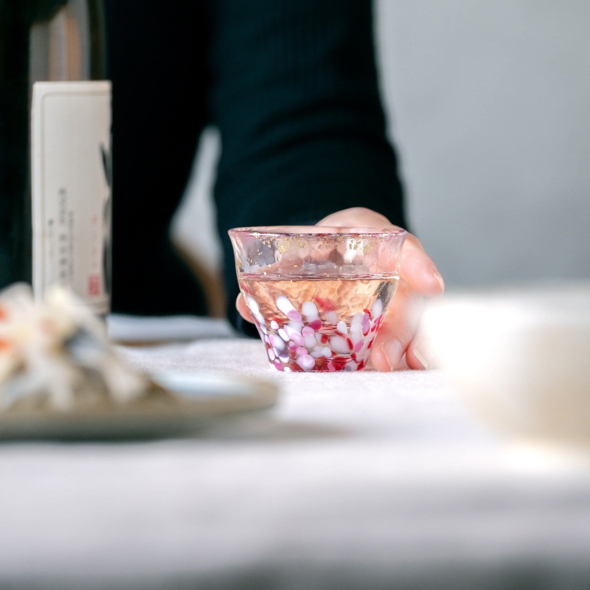 津軽びいどろ 金彩ぐいのみ こぼれ桜 日本酒が注がれたおちょこをつかんでいる画像