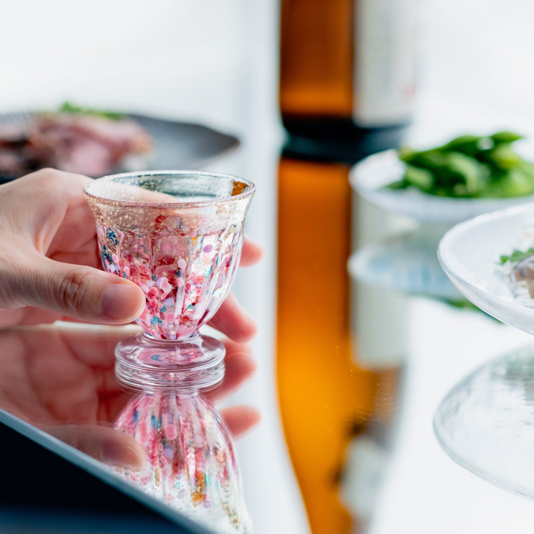 津軽びいどろ 盃12ヶ月コレクション 2月春時雨 食卓に並ぶ盃を手でつかんでいる画像