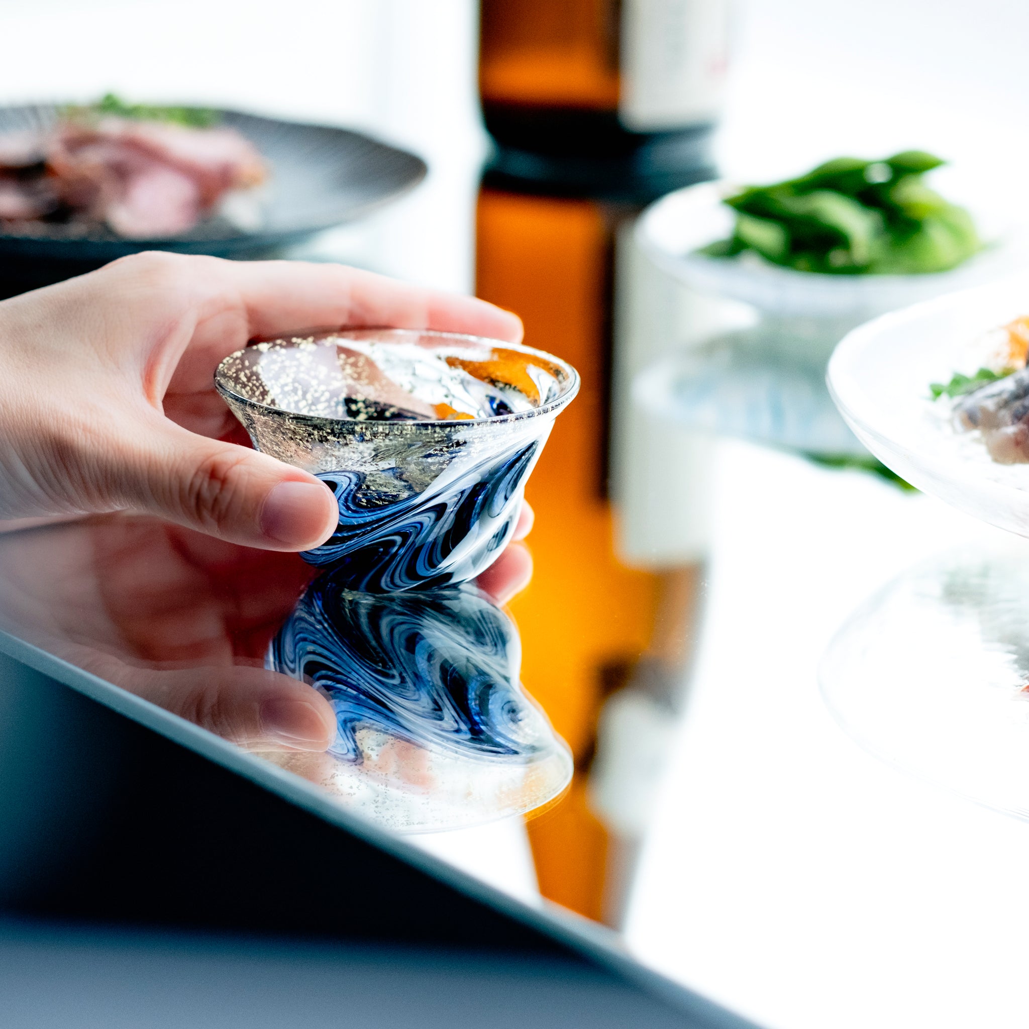 津軽びいどろ 盃12ヶ月コレクション 8月天の川 食卓に並ぶ盃を手でつかんでいる画像