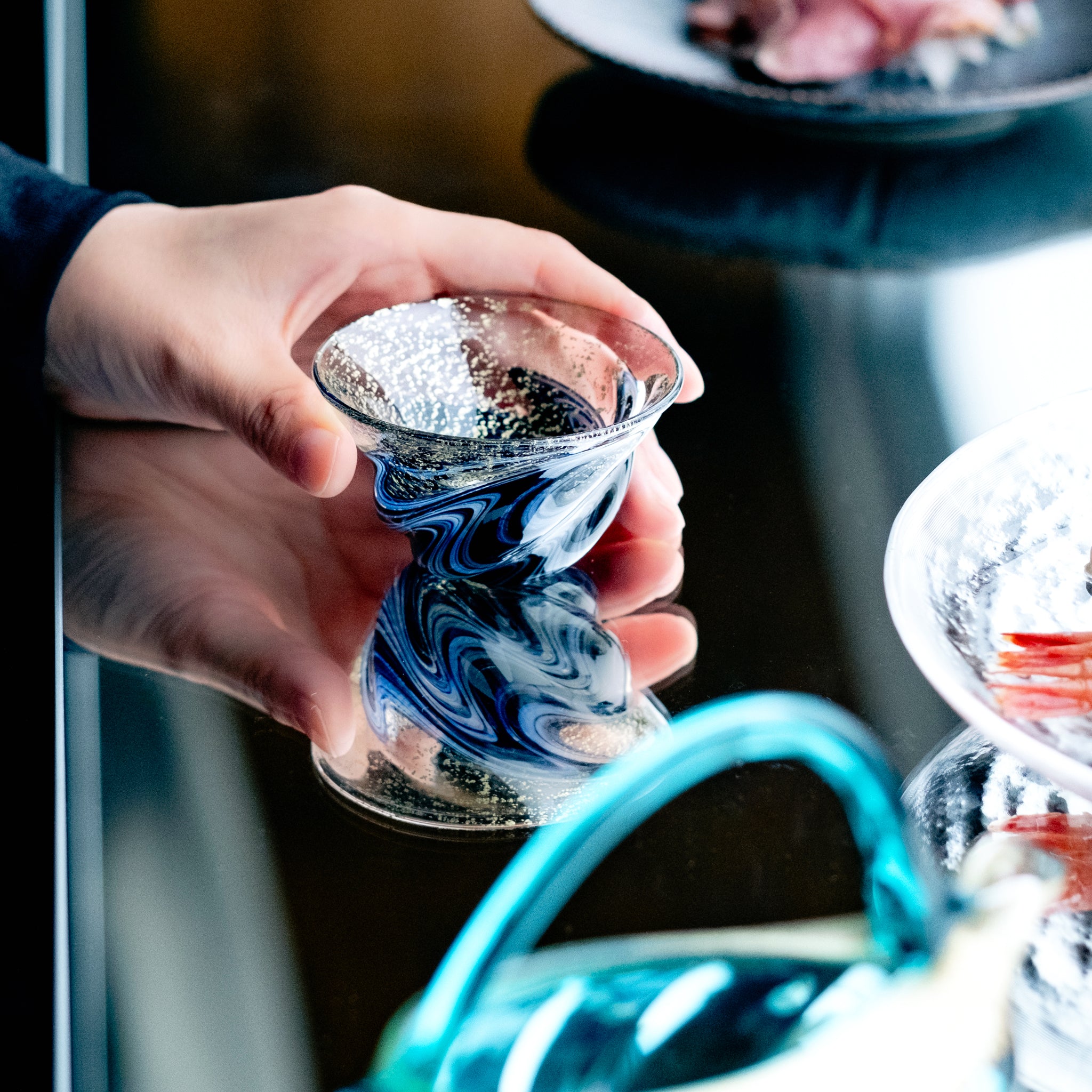 津軽びいどろ 盃12ヶ月コレクション 8月天の川 食卓に並ぶ盃を手でつかんでいる画像