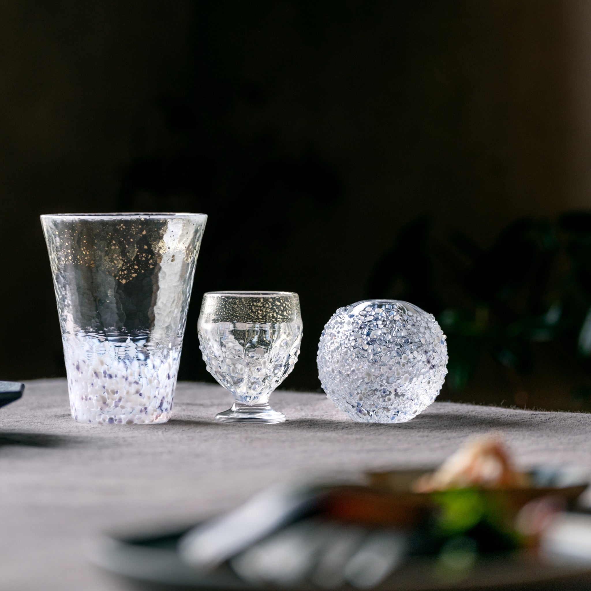 販路限定】津軽びいどろ 雪うつし つぶ雪 盃 雪を表現したグラスやおちょこがテーブルに並んでいる画像