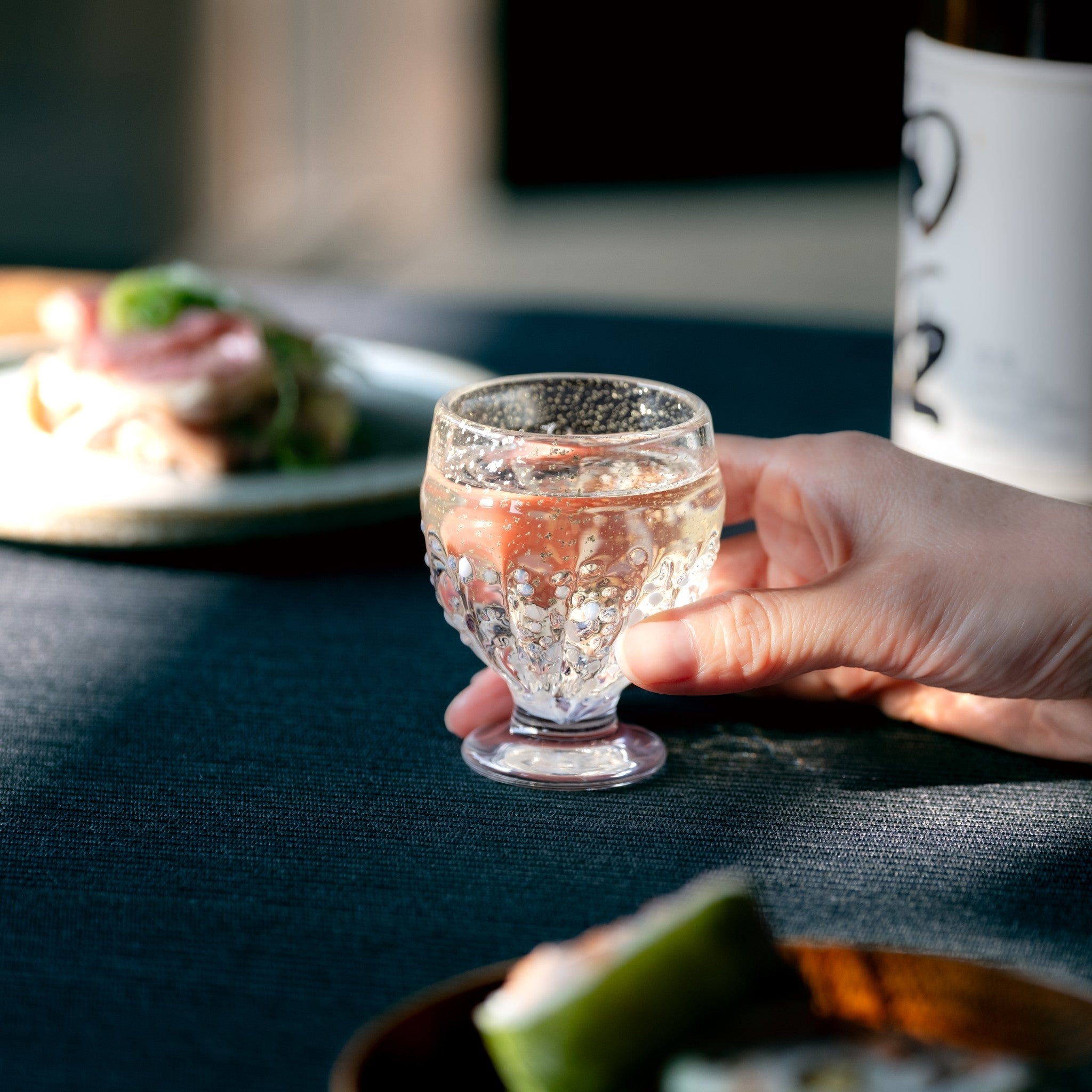 【販路限定】津軽びいどろ 雪うつし つぶ雪 盃 脚付きのおちょこを手でつかんでいる画像