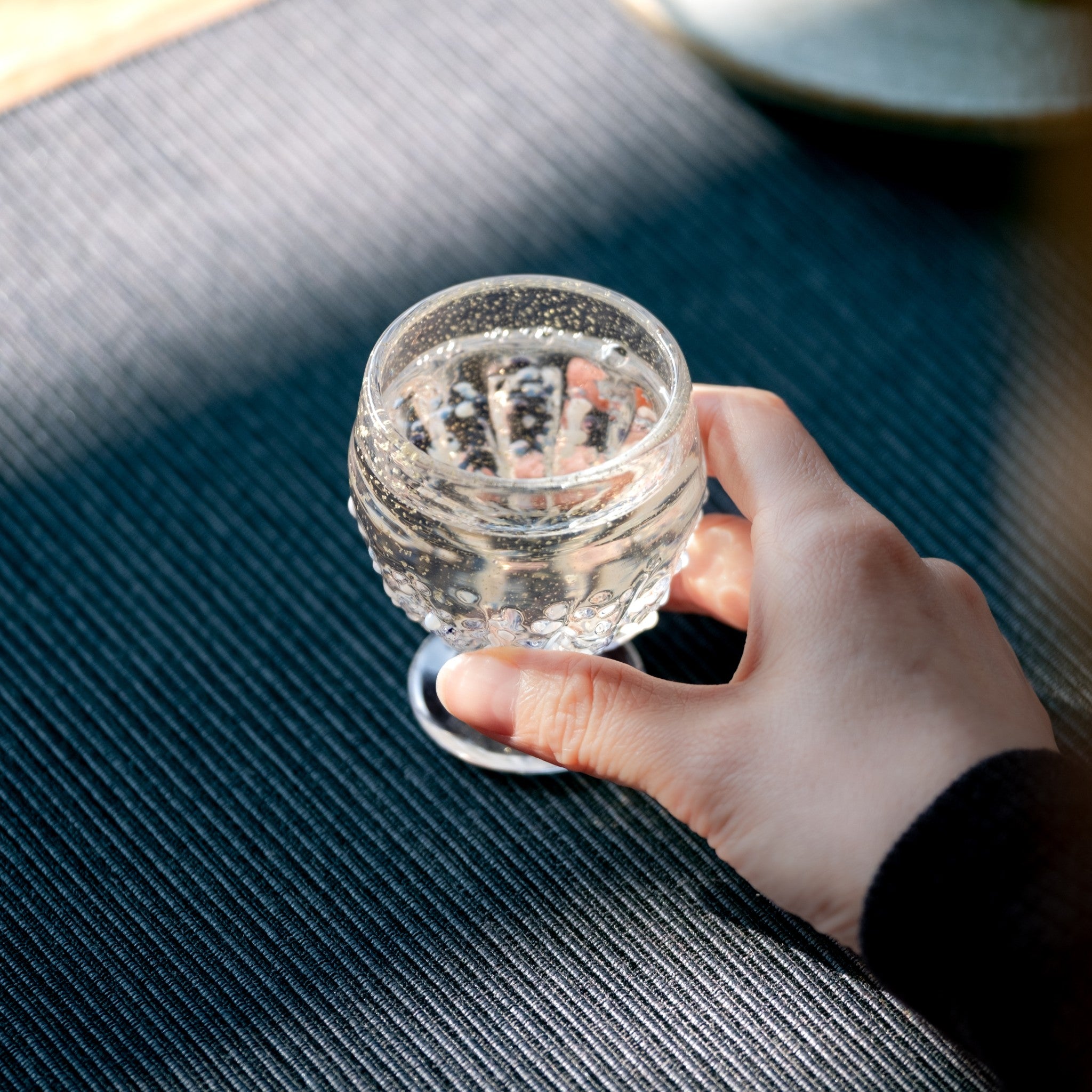 【販路限定】津軽びいどろ 雪うつし つぶ雪 盃 透き通ったガラスのおちょこを手でつかんでいる画像