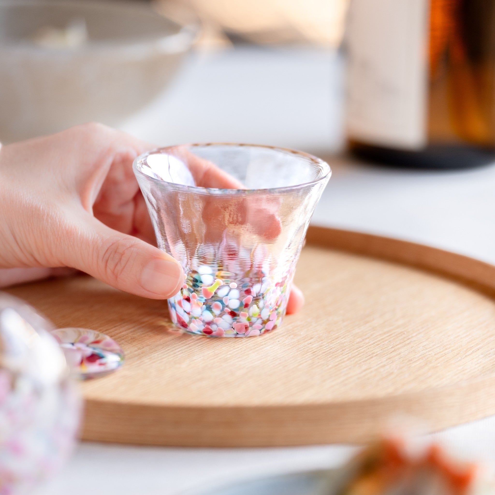 津軽びいどろ にほんの色 ふうけい 盃 春の丘 ハンドメイドのがらすおちょこを手でつかんでいる画像