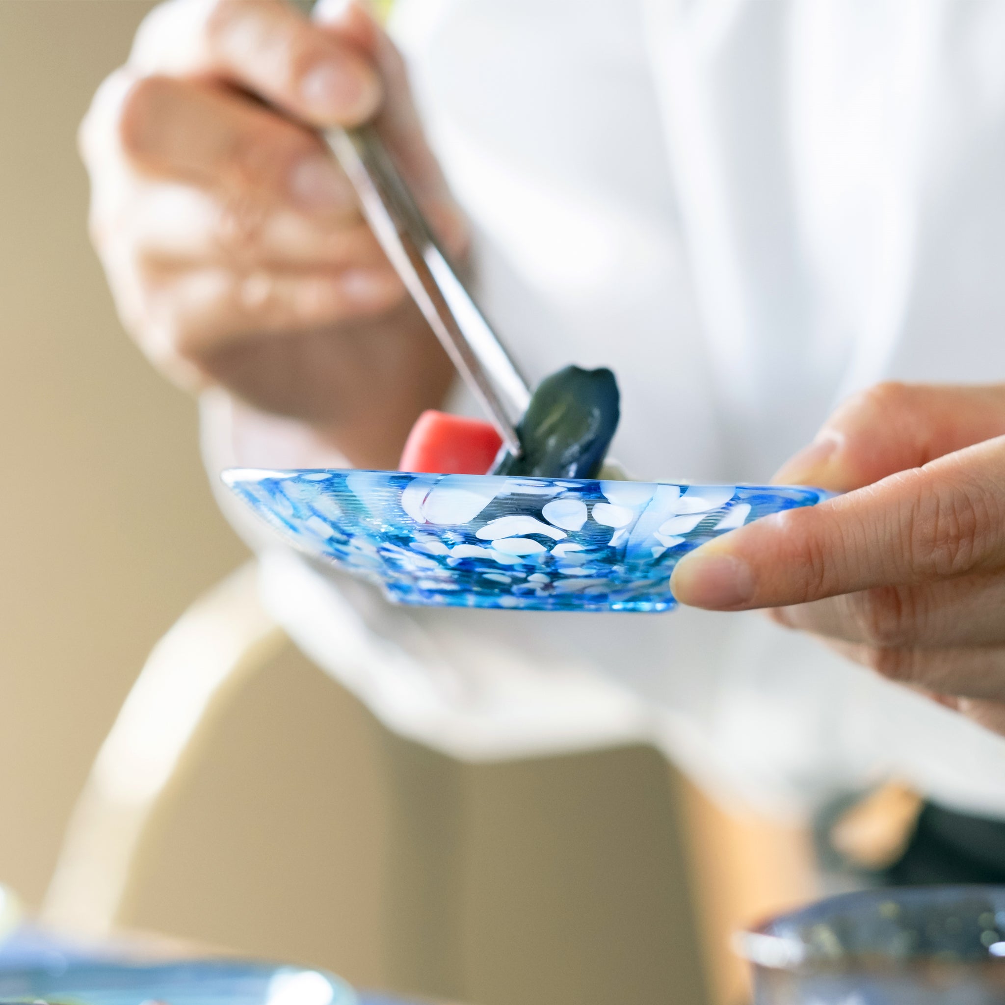 津軽びいどろ 色色豆皿 あじさい 料理が乗った小皿を手で持ち上げている画像