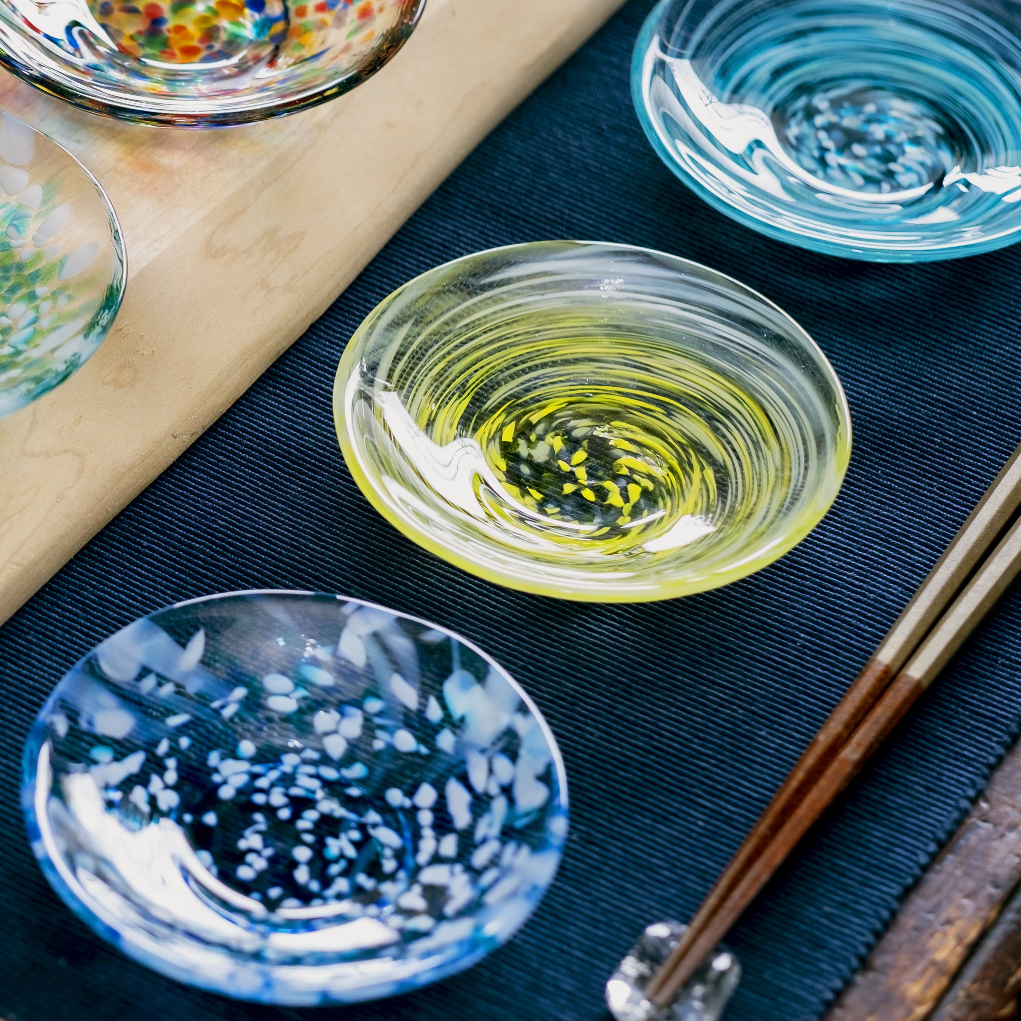 津軽びいどろ 色色豆皿 菜の花 色違いの小皿がテーブルに並んでいる画像