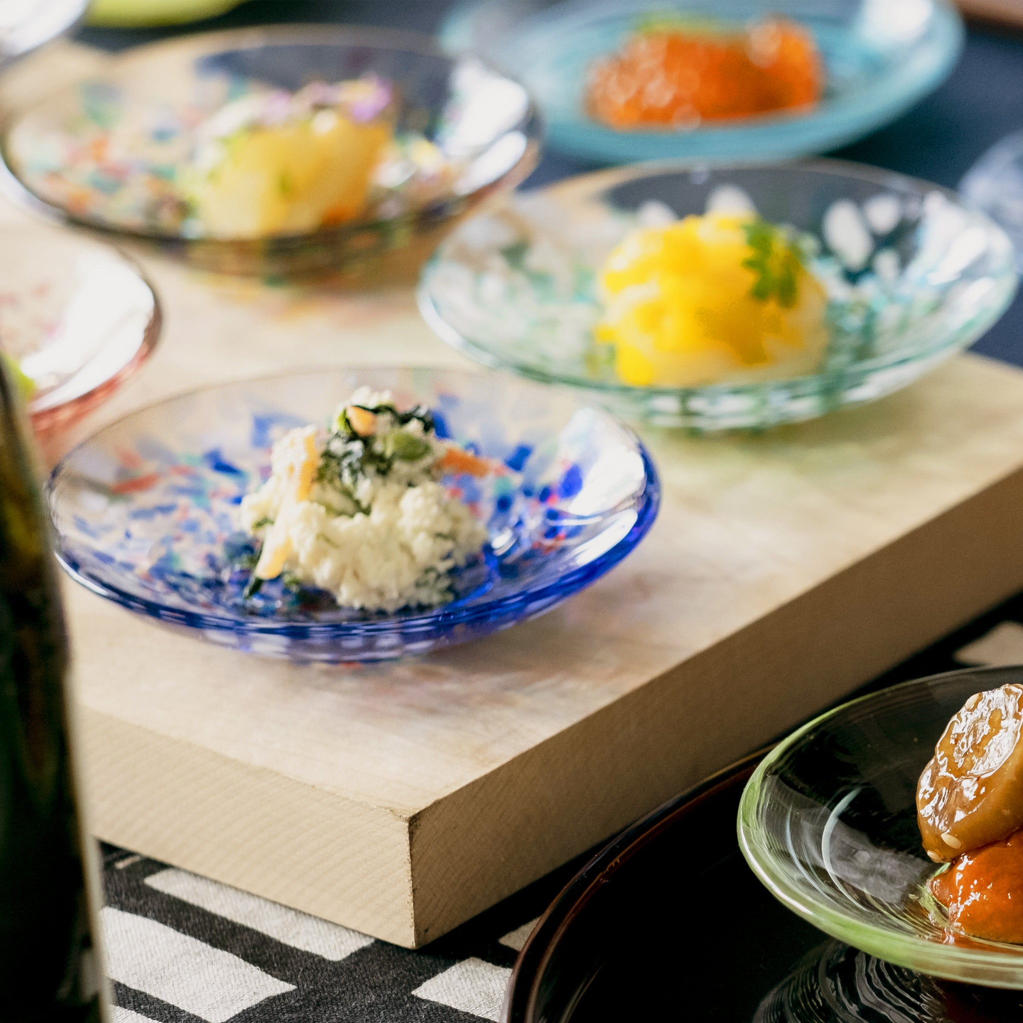 津軽びいどろ 色色豆皿 夏海 料理が乗った色違いの小皿が食卓に並んでいる画像