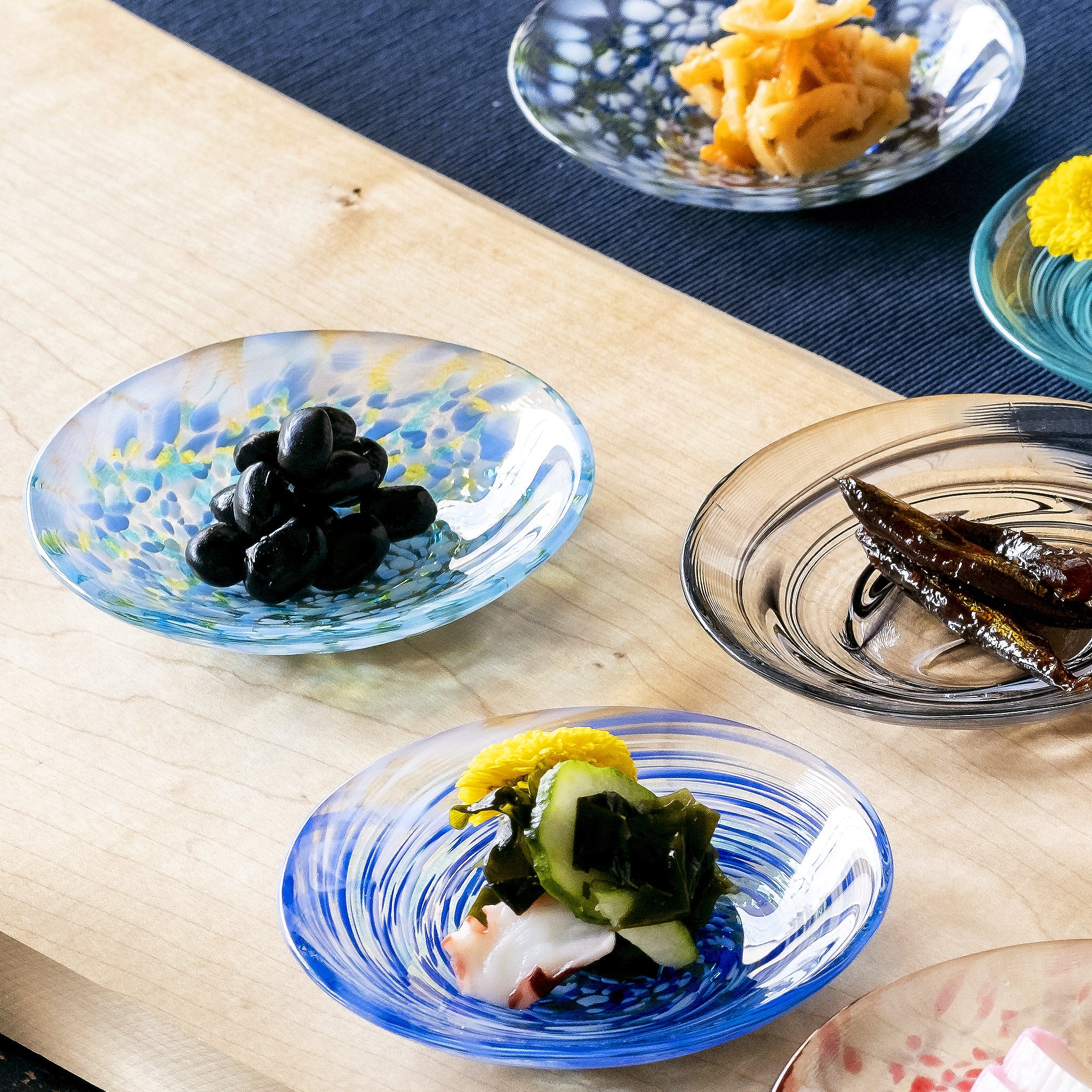 津軽びいどろ 色色豆皿 水鞠 料理が乗った色違いの小皿がテーブルに並んでいる画像
