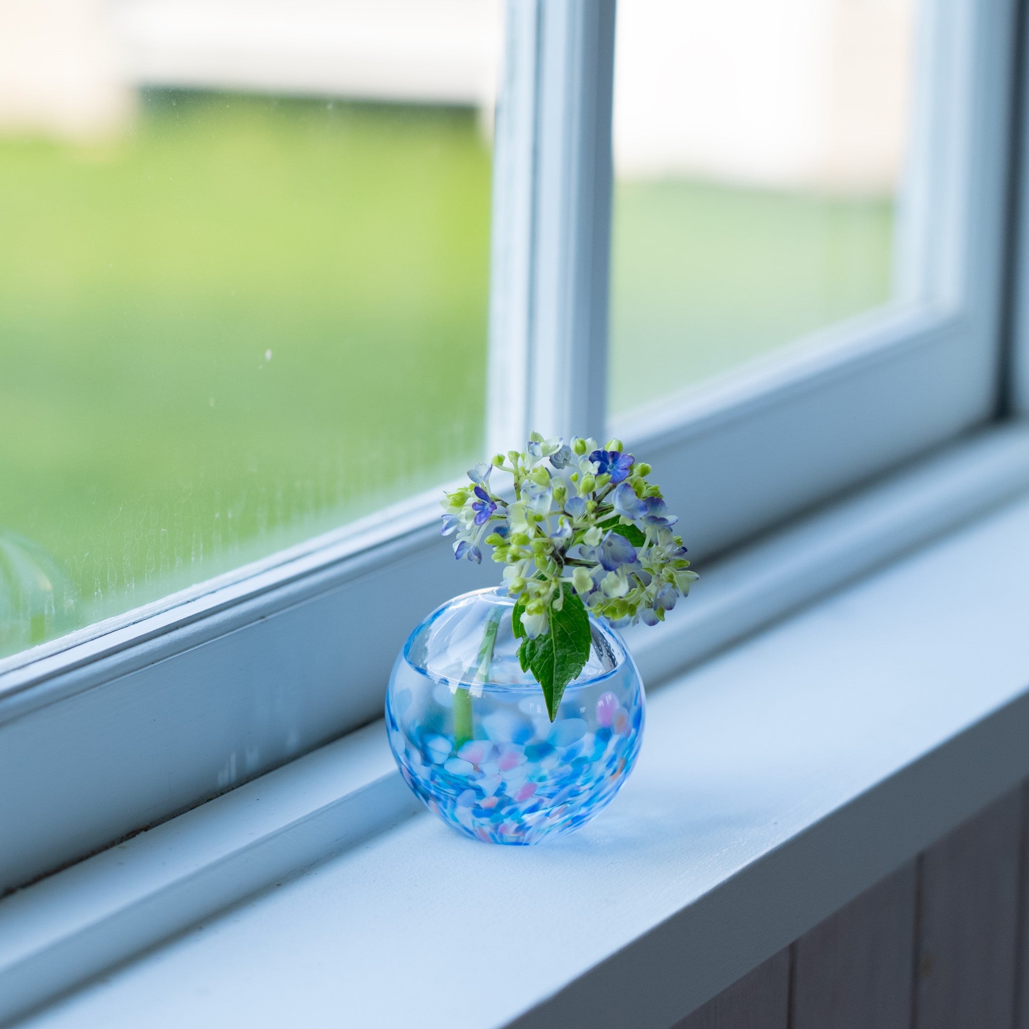 津軽びいどろ にほんの色 ふうけい 一輪挿し 夕凪の空 窓際に置かれている丸い花瓶の画像