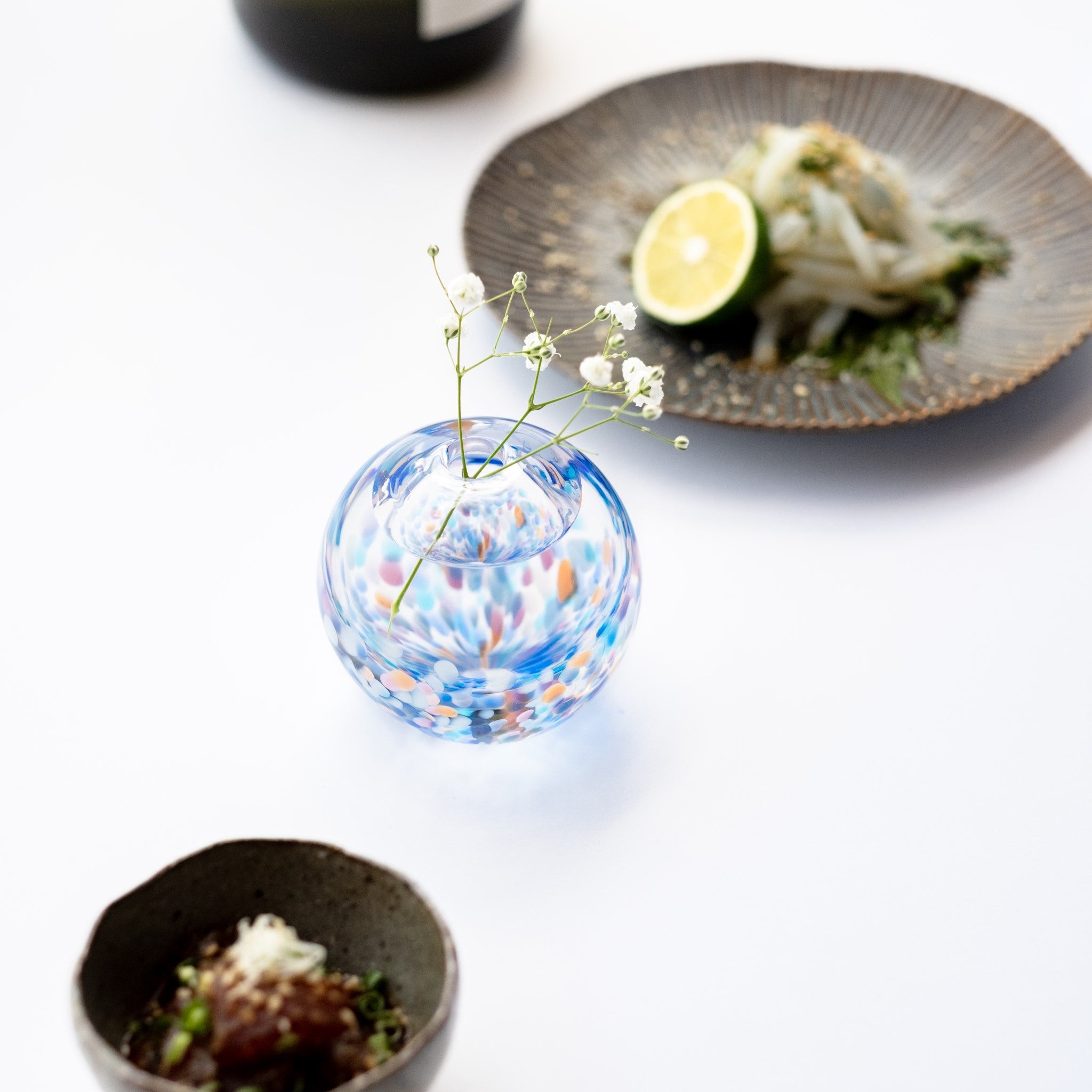 津軽びいどろ にほんの色 ふうけい 一輪挿し 夕凪の空 丸い花瓶に花が活けられている画像