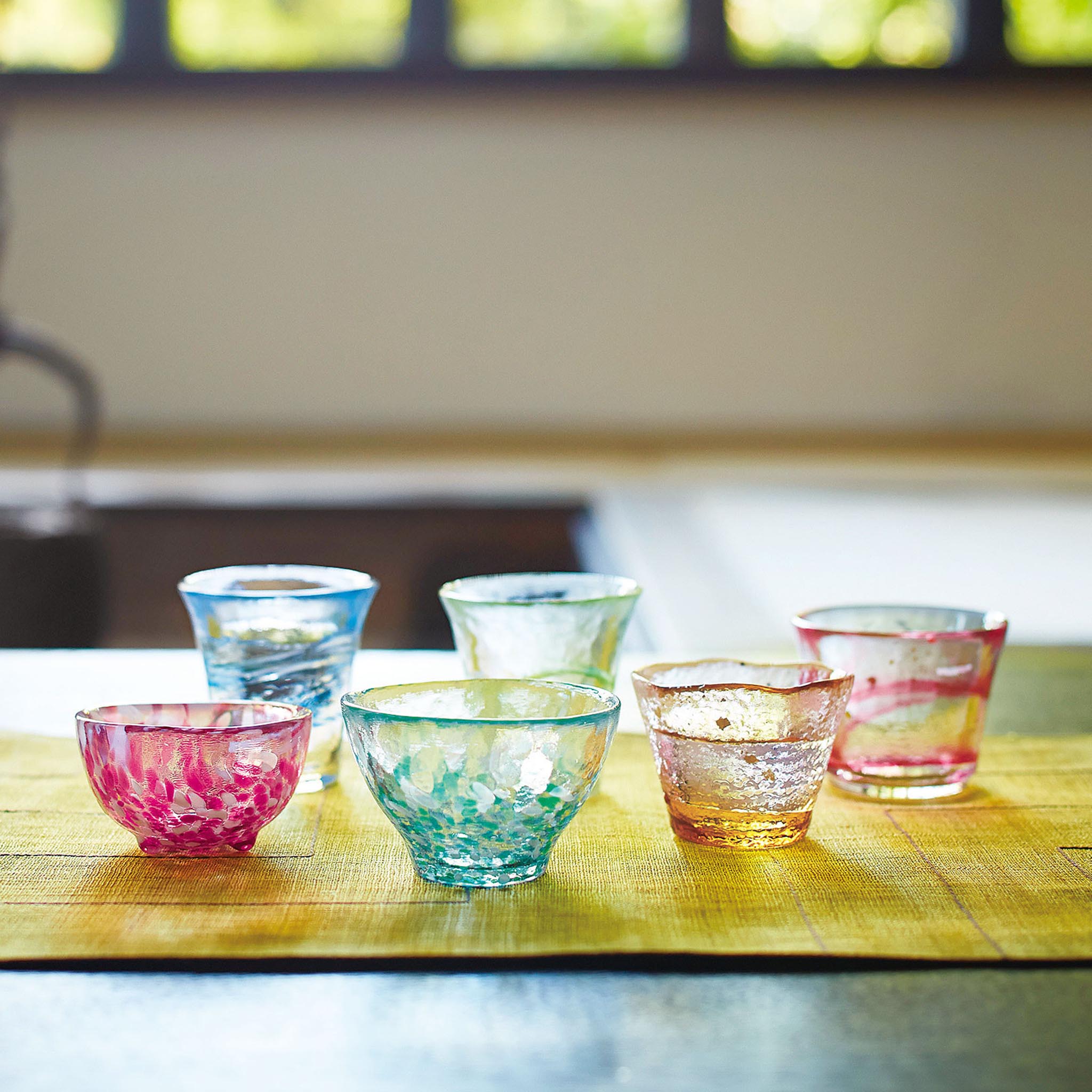 津軽びいどろ 盃コレクション 盃みずばしょう 様々な形の盃がテーブルに並んでいる画像