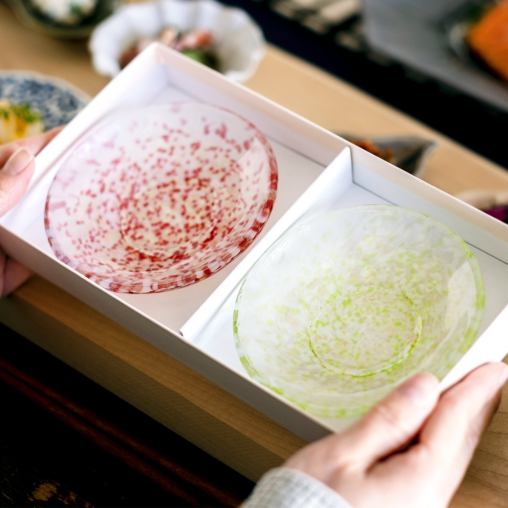 津軽びいどろ 豆皿ギフト りんご豆皿ペアセット ガラスの器が入った化粧箱を手で持ち上げている画像