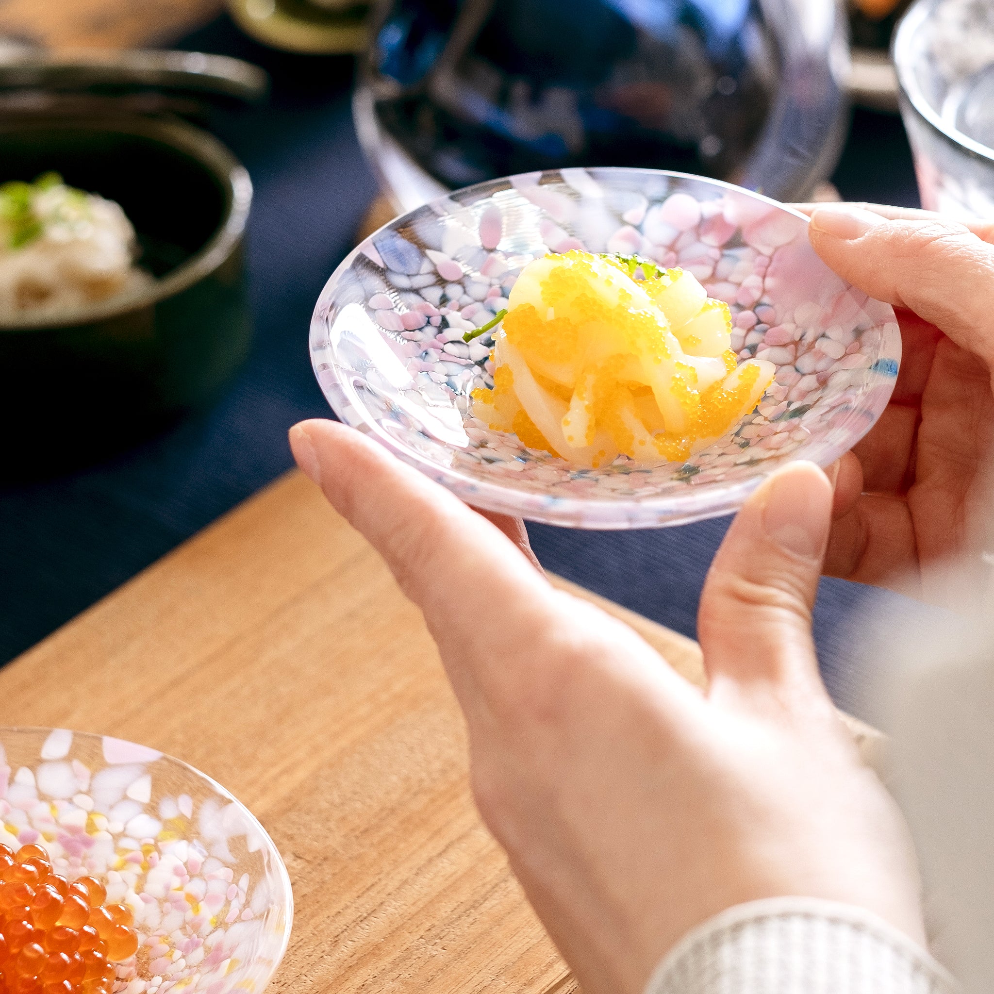 津軽びいどろ 豆皿ギフト SAKURAペアセット菜の花と青い空 料理がよそわれたガラス食器を持ち上げている画像