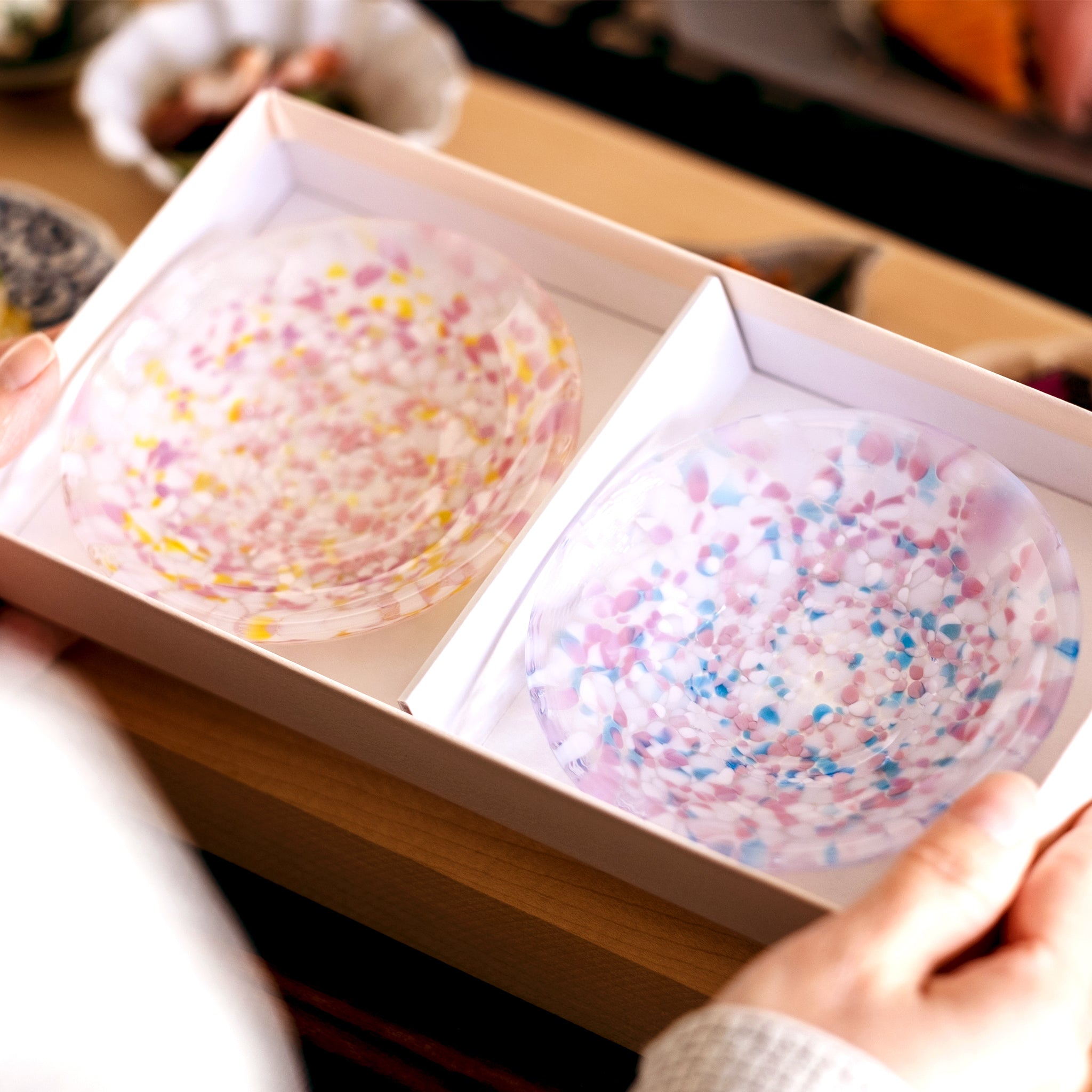 津軽びいどろ 豆皿ギフト SAKURAペアセット菜の花と青い空 ガラス食器が入った化粧箱を手で持ち上げている画像
