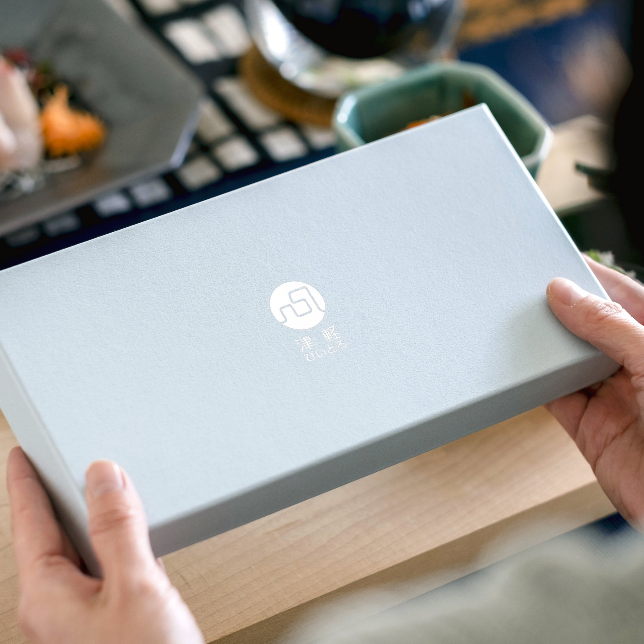 津軽びいどろ 豆皿ギフト MATSURI金彩ペアセット 化粧箱を手で持ち上げている画像