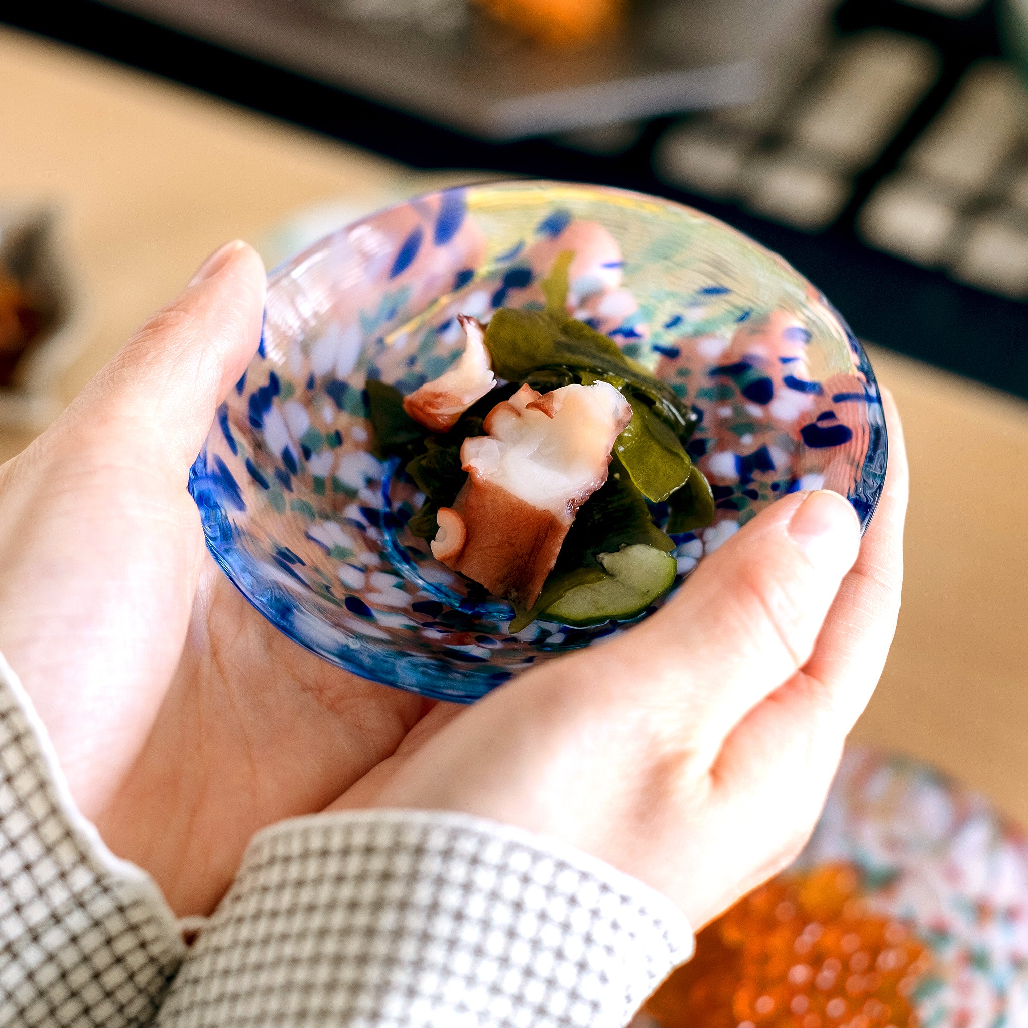 津軽びいどろ 豆皿ギフト 色色豆皿彩合わせセット タコの酢の物をよそったガラス食器を手で持ち上げている画像