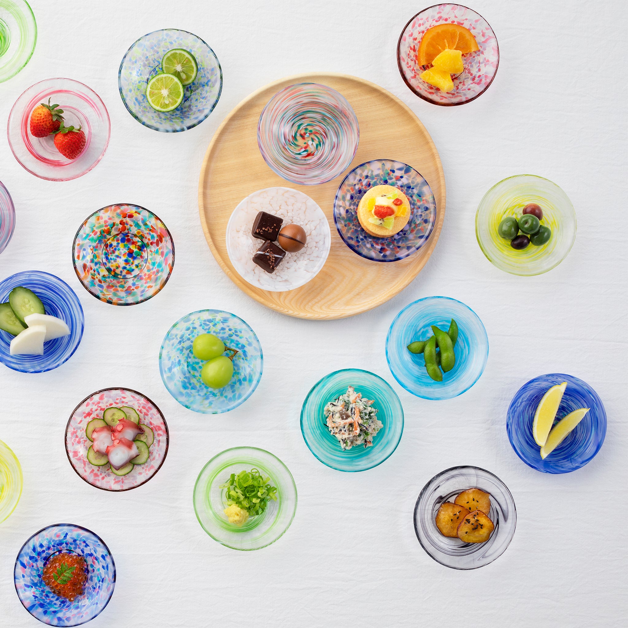 津軽びいどろ 色色豆皿 夏海 お菓子や料理が乗った色違いの小皿がテーブルにたくさん並んでいる画像