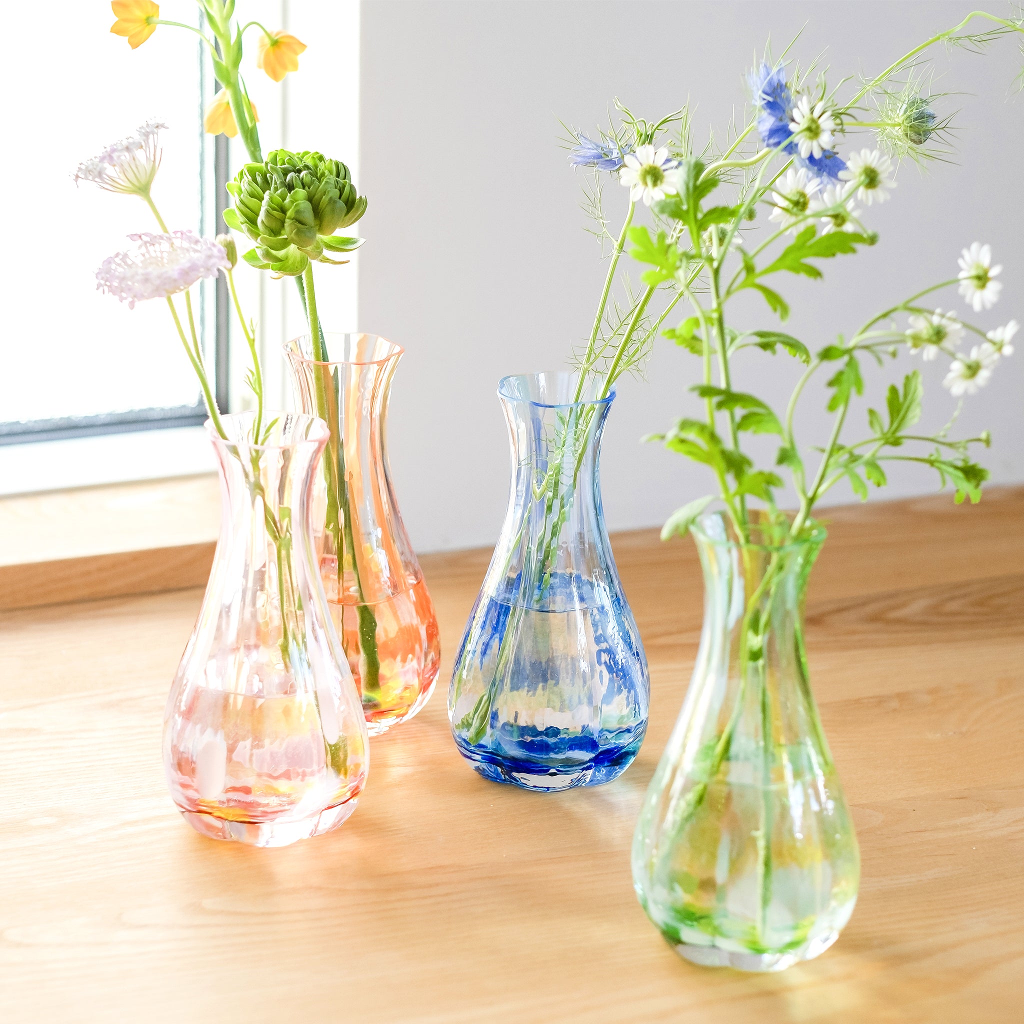 津軽びいどろ 花ひかり シーブルー 色違いの花器が窓際に並んでいる画像