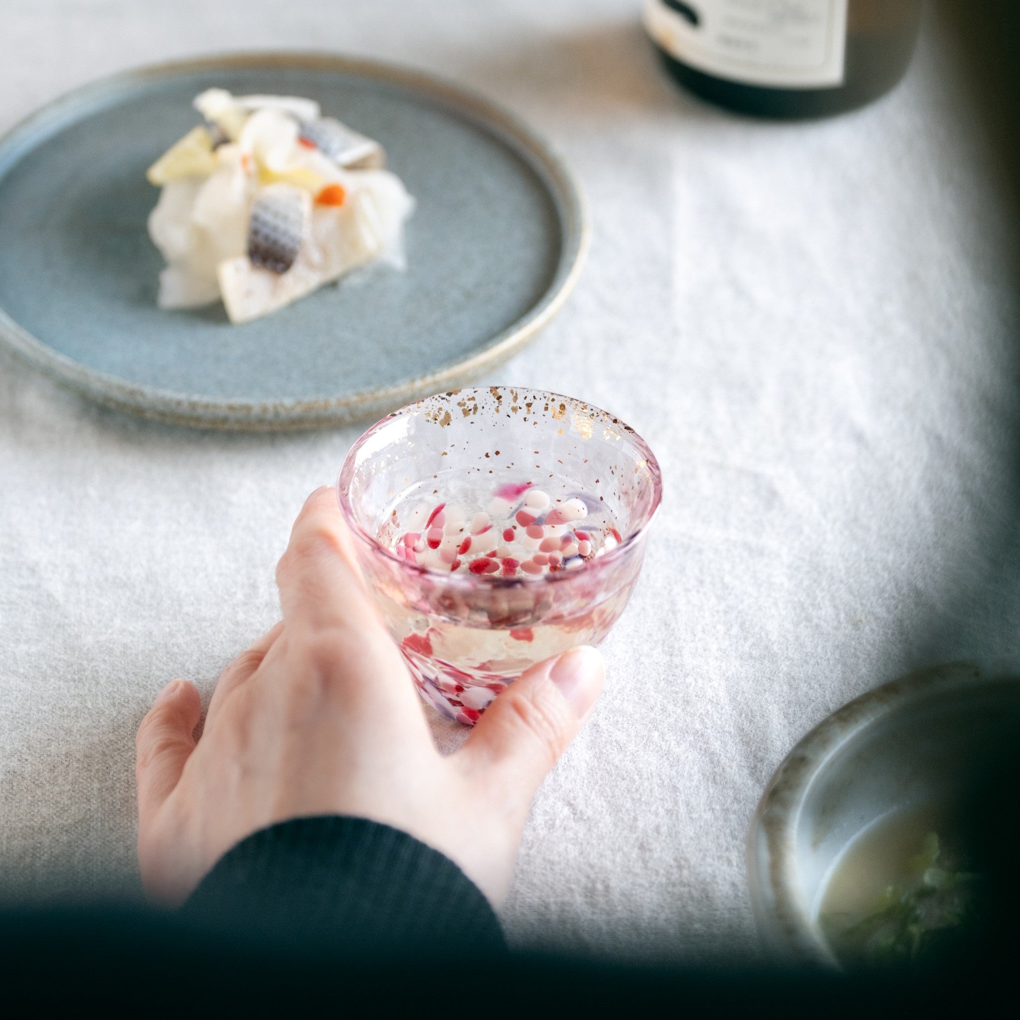 津軽びいどろ 金彩ぐいのみ こぼれ桜 日本酒が注がれたハンドメイドのガラスおちょこを手でつかんでいる画像