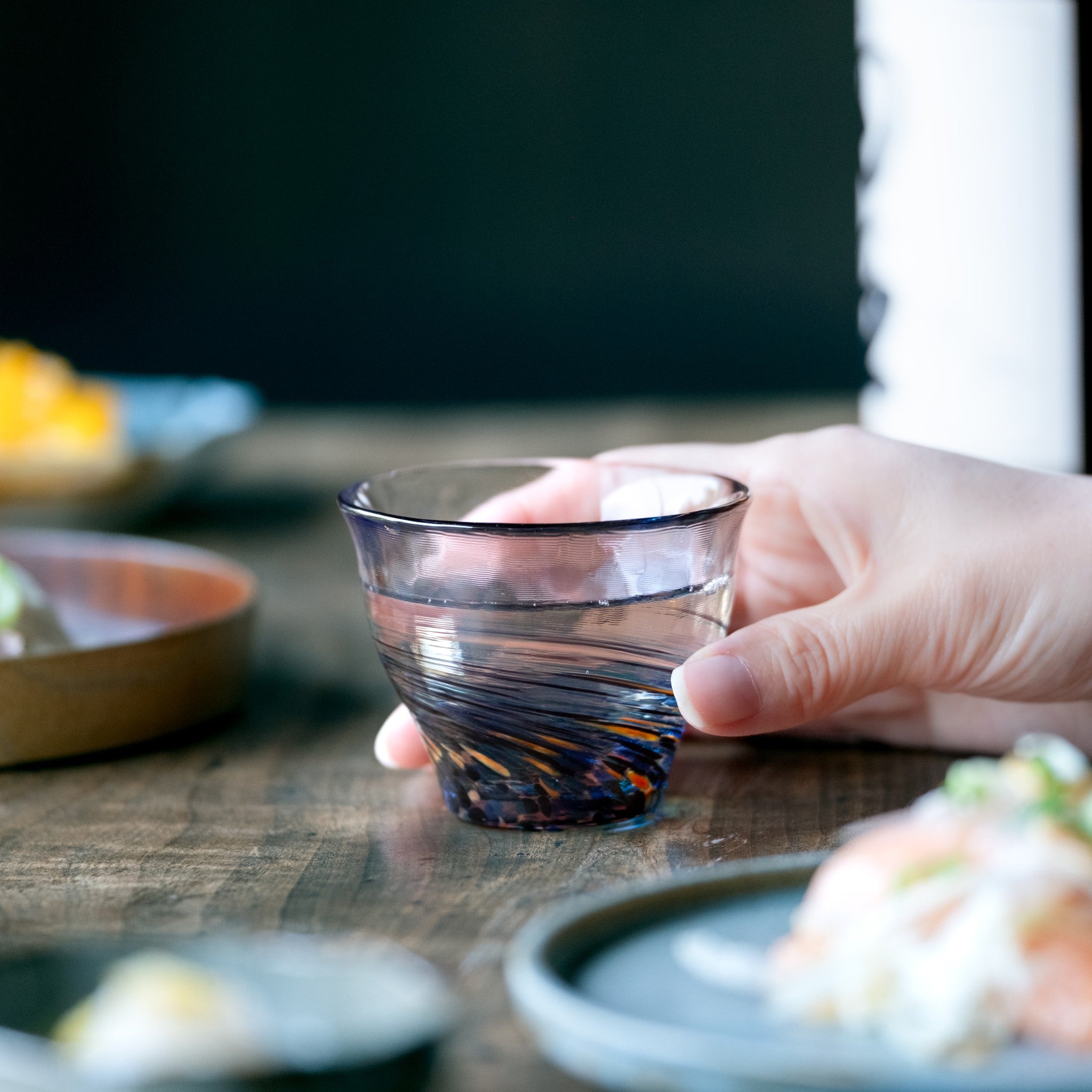 津軽びいどろ 六の色(むつのいろ) 盃ペア 雪と夜 日本酒が注がれたおちょこを手でつかんでいる画像