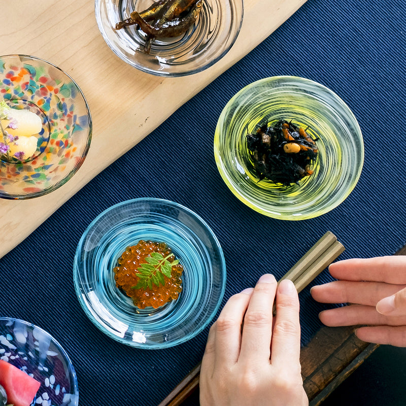  津軽びいどろ 色色豆皿 菜の花 料理乗った色違いの小皿がテーブルに並んでいる画像