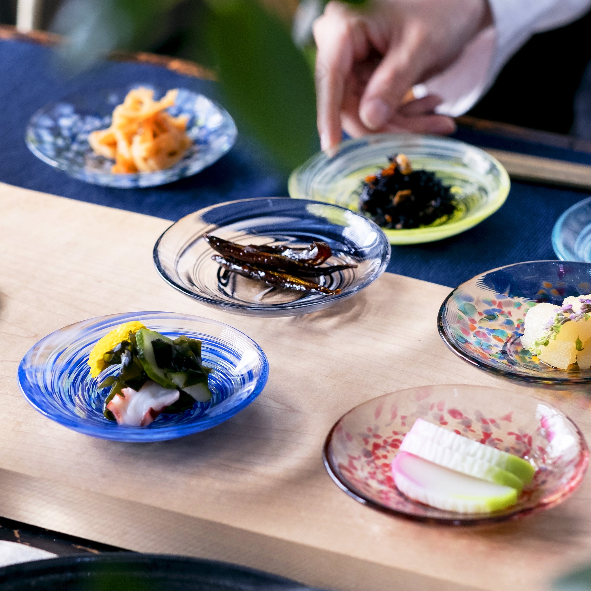  津軽びいどろ 色色豆皿 紺青 料理が乗った小皿に手を添えている画像