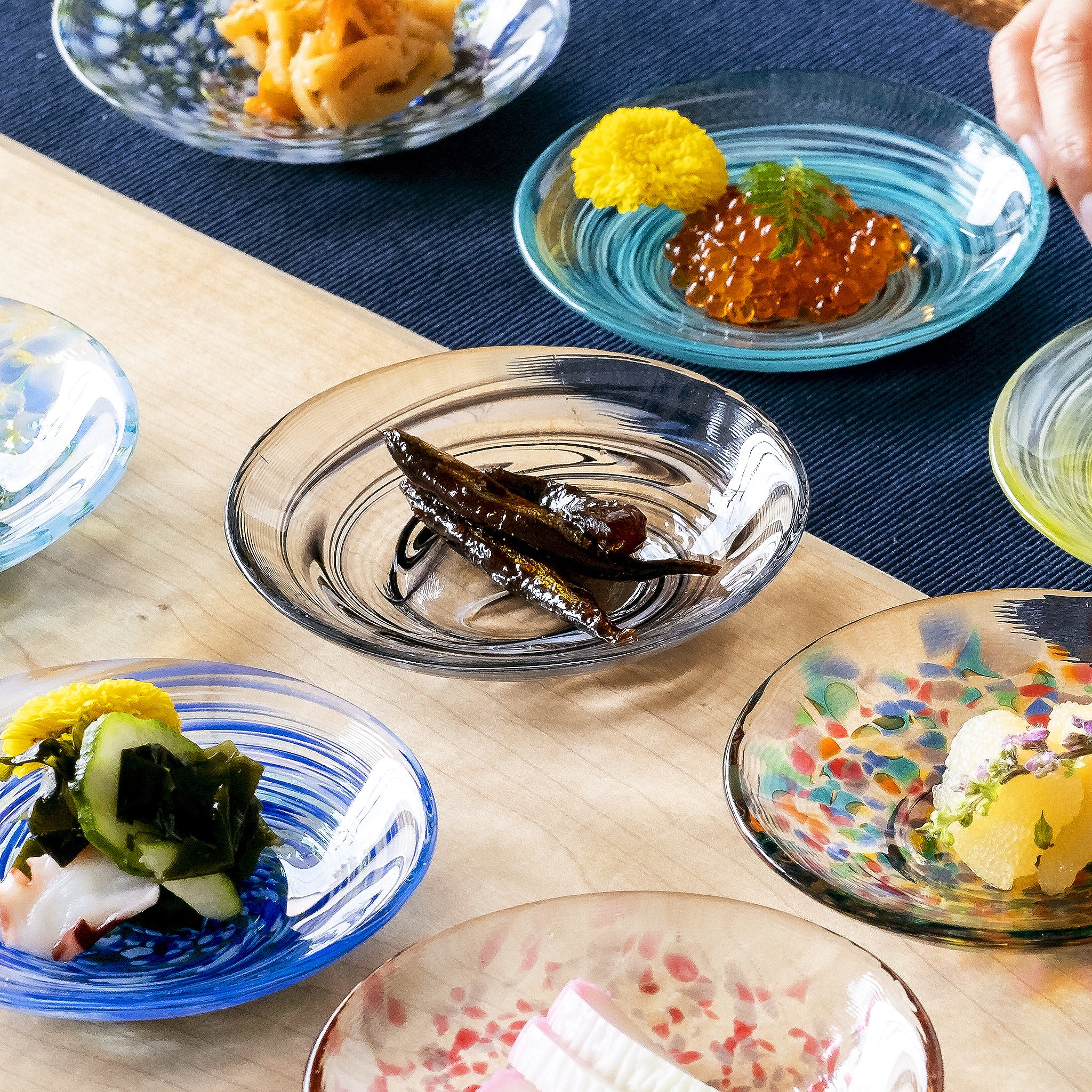 津軽びいどろ 色色豆皿 夜雲 料理が乗った色違いの小皿が食卓に並んでいる画像