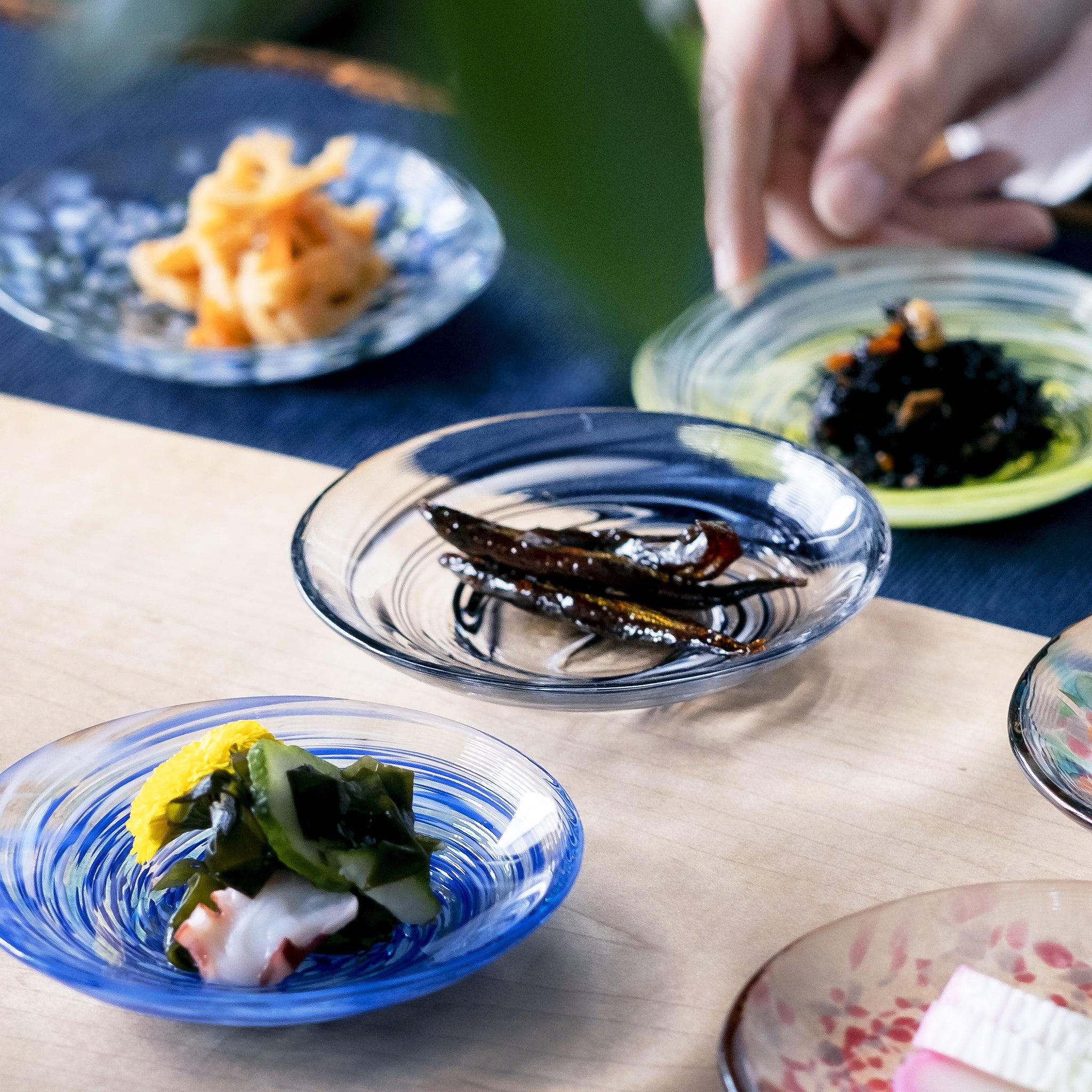  津軽びいどろ 色色豆皿 夜雲 料理が乗った小皿に手を添えている画像