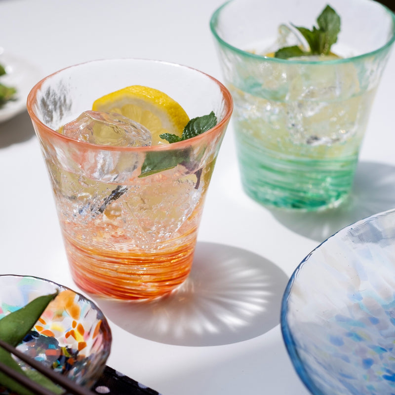 津軽びいどろ 12色のグラス 紅  レモン水が注がれた色違いのグラスが食卓に並んでいる画像