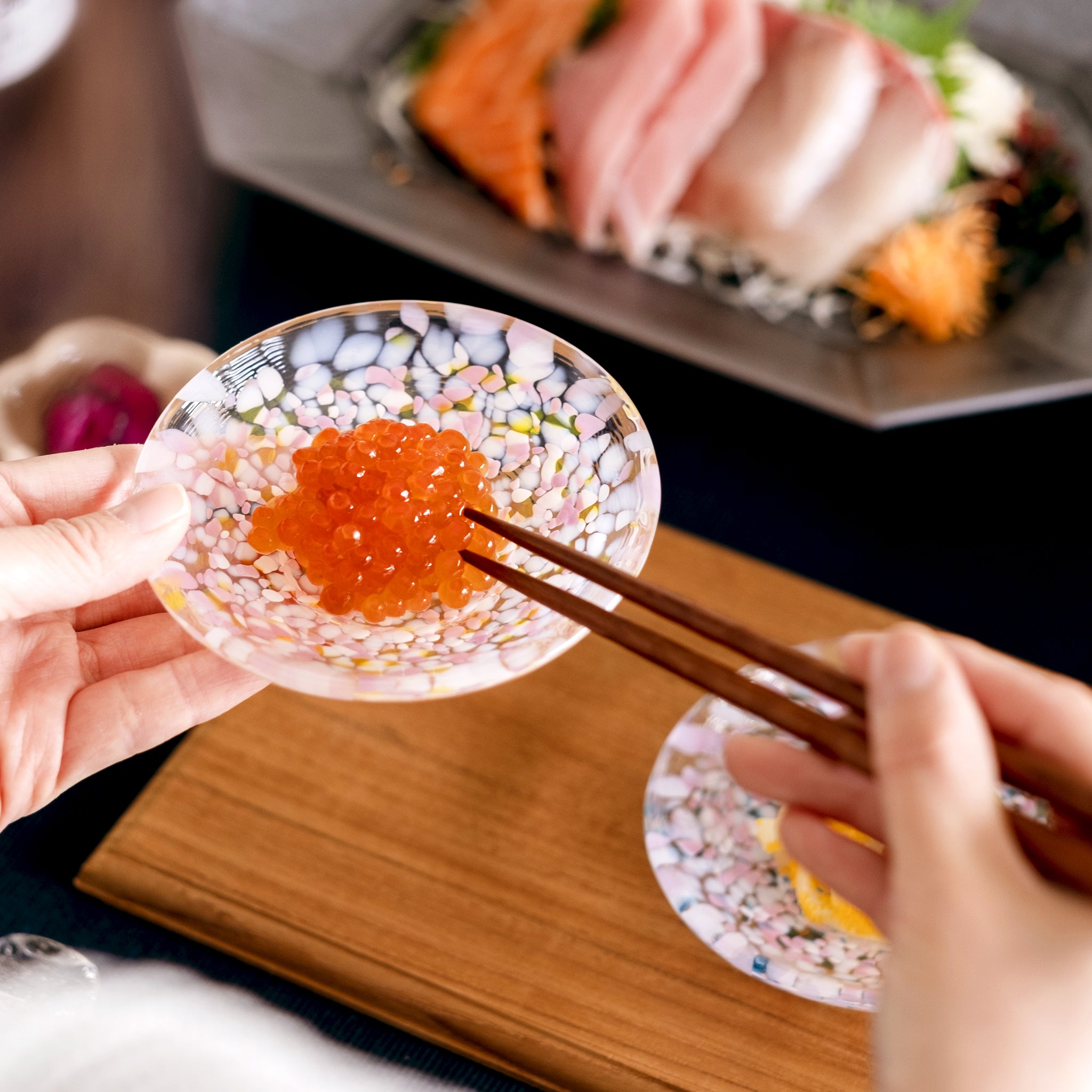 津軽びいどろ 豆皿ギフト  SAKURAペアセット菜の花と青い空　いくらがよそわれたガラス食器を手で持ち上げている画像