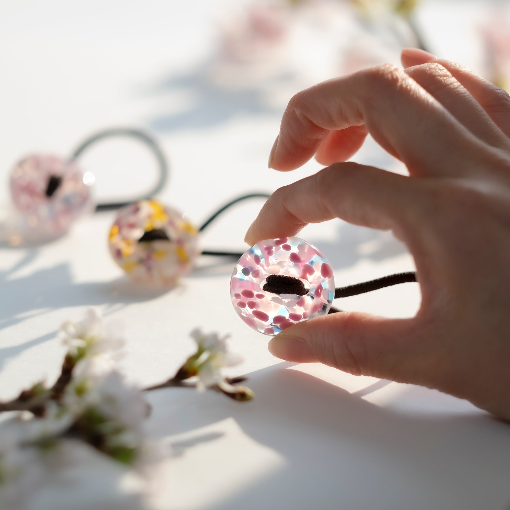 津軽びいどろ さくらさくら ヘアゴム桜と青い空 ヘアゴムを手でつかんでいる画像