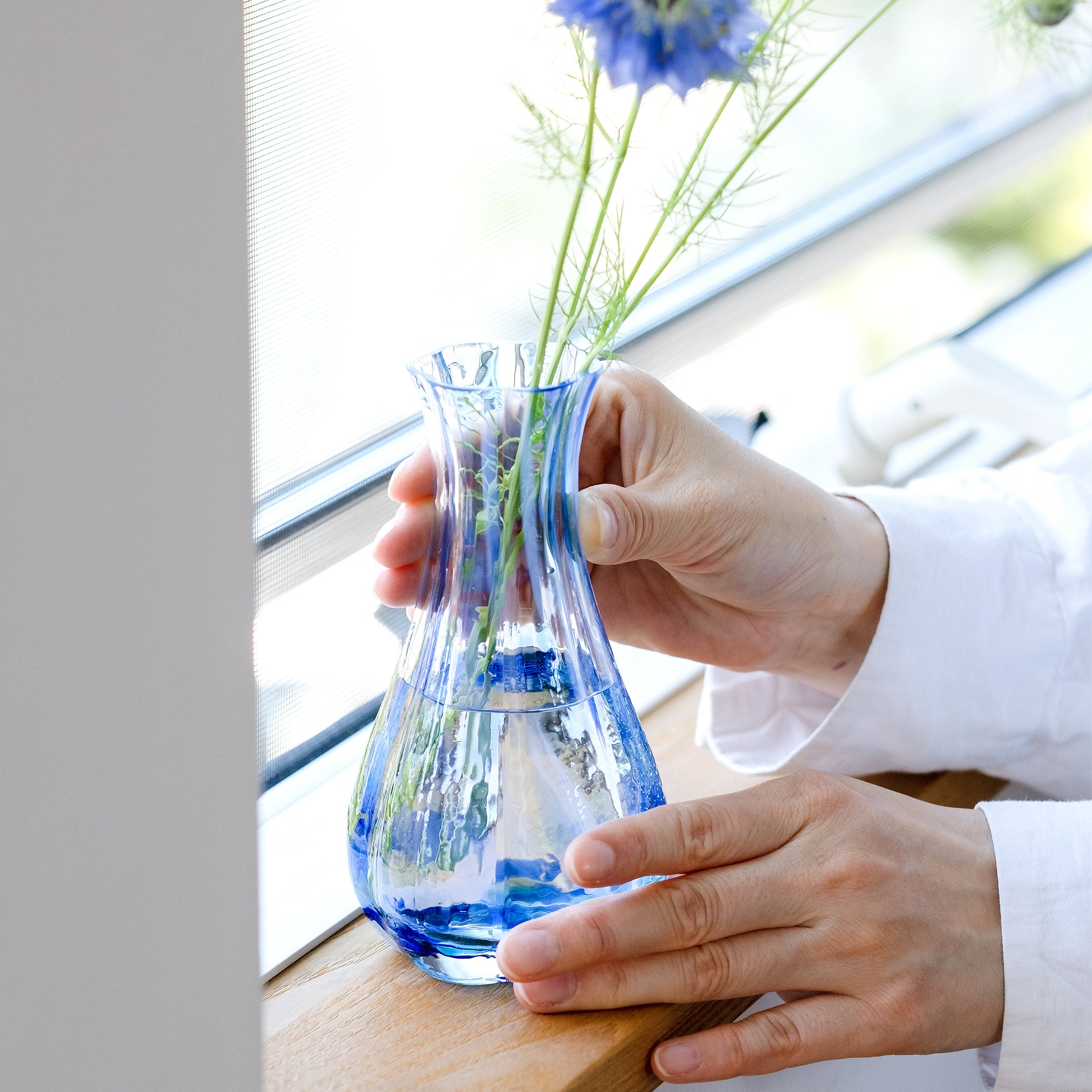 津軽びいどろ 花ひかり シーブルー 手が添えられている花器の画像